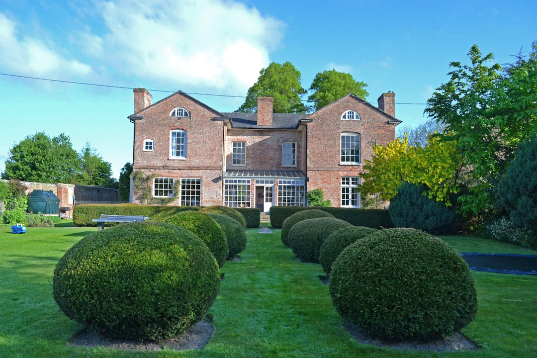 a large brick house with a lawn and hedges in front of it with Moseley Old Hall in the background